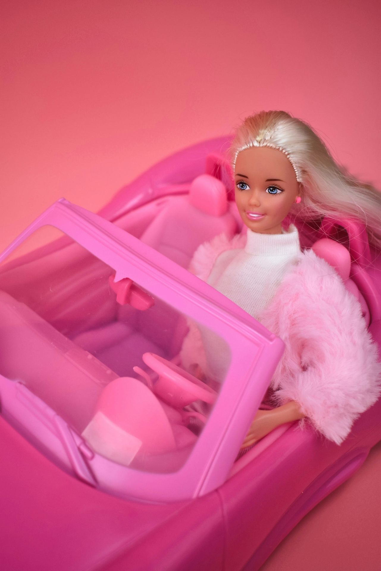 A barbie doll sitting in a pink car